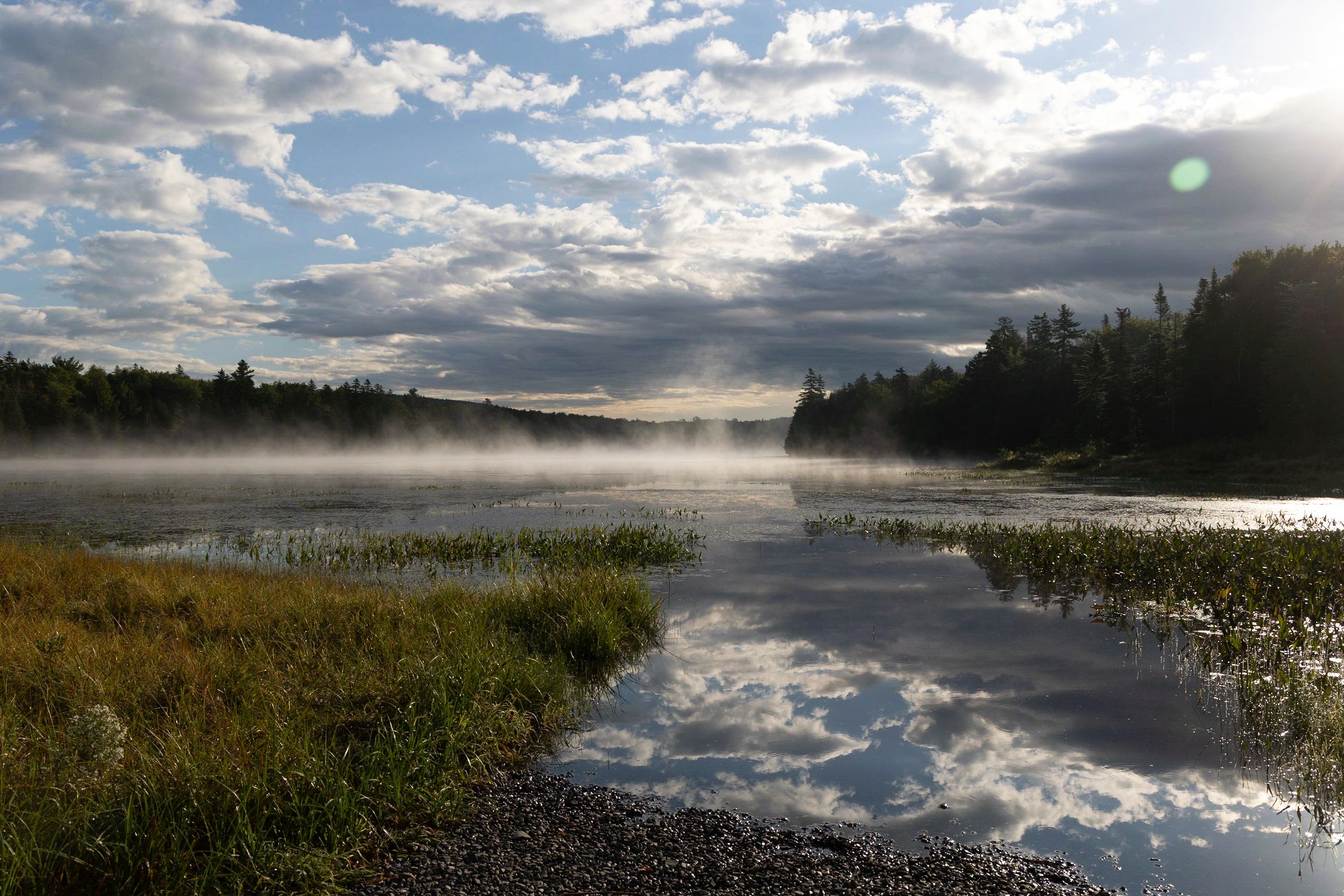 Stunning reflection of the early morning sky in a still lake as the early morning Maine fog burns off