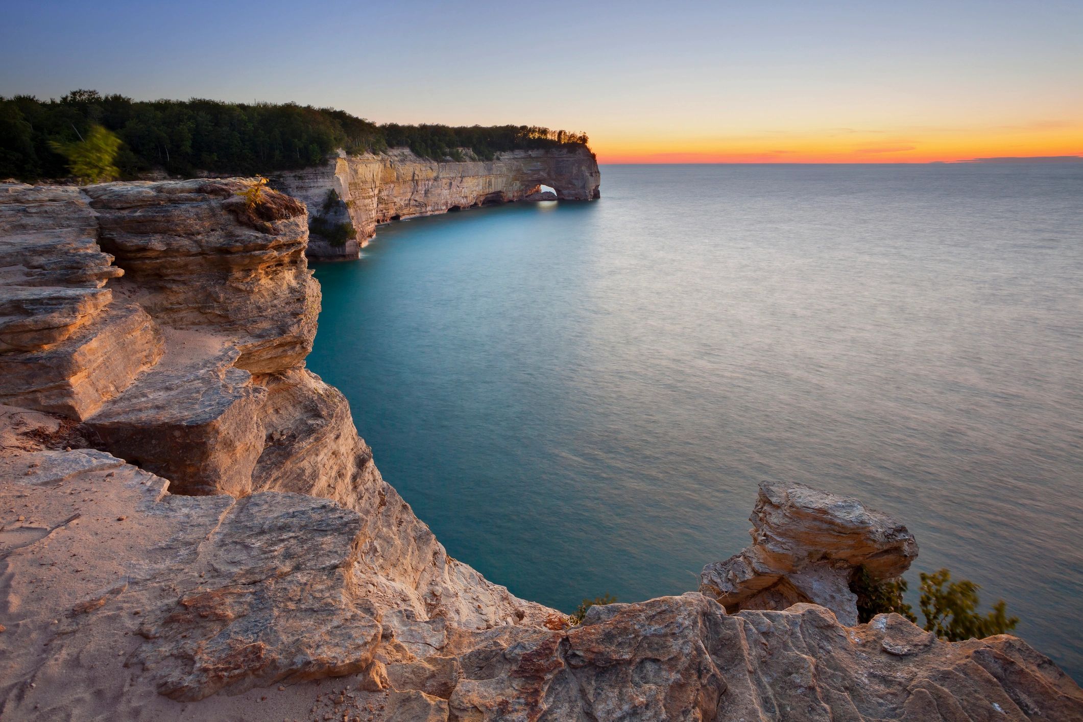 Wide shot of rocks looking over sea at sunset in Michigan