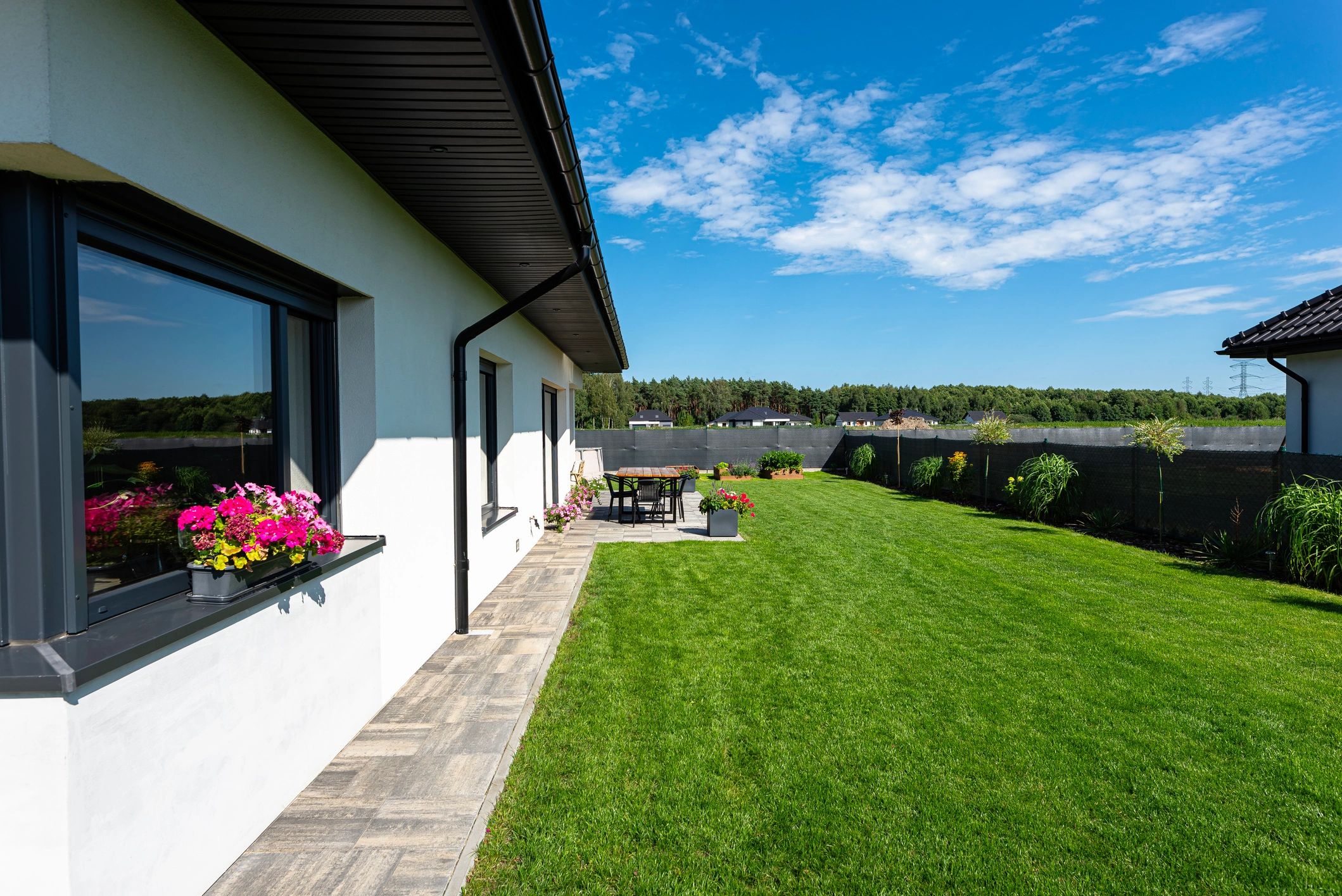 Beautiful garden with green grass, visible terrace table and house in beautiful summer weather, very wide shot.