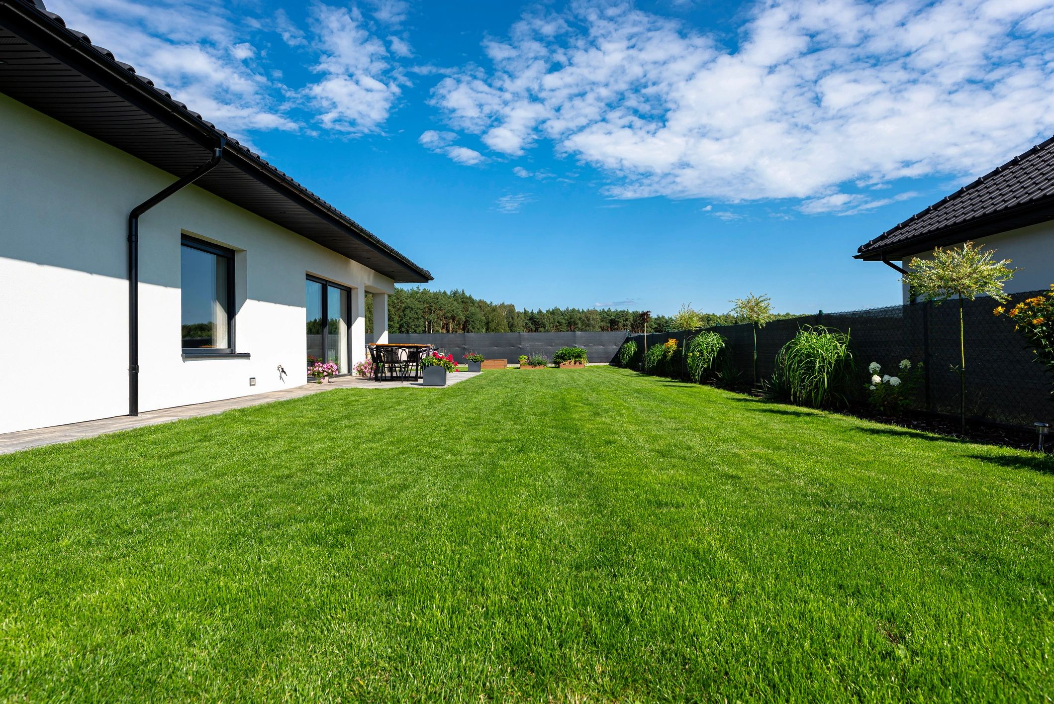 Beautiful garden with green grass, visible terrace table and house in beautiful summer weather, very wide shot.