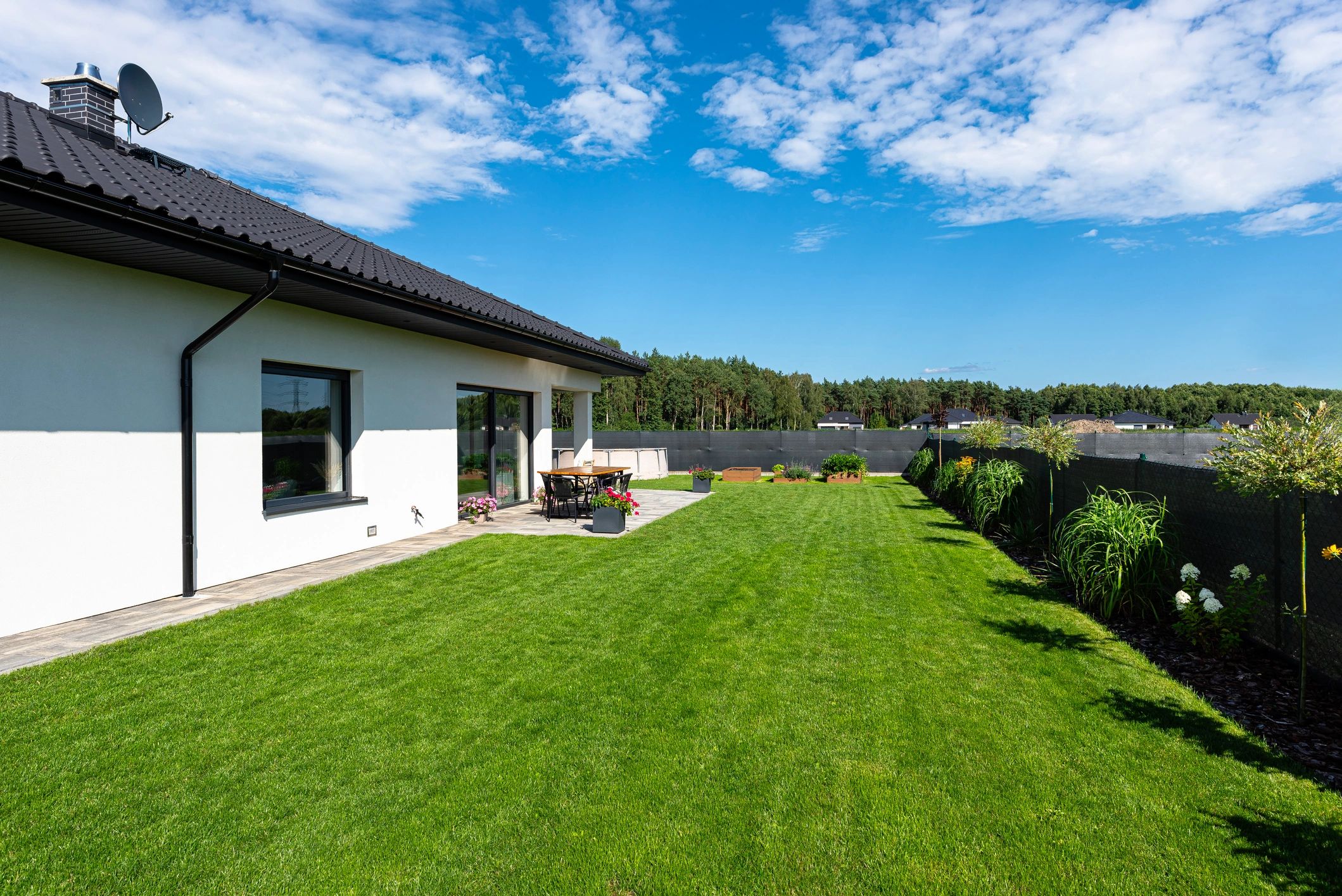Beautiful garden with green grass, visible terrace table and house in beautiful summer weather, very wide shot.